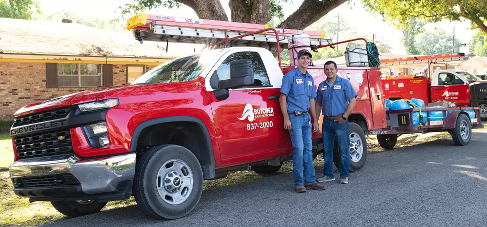 Image of Butcher Air Conditioning technicians standing in front of the company truck on an AC service job site.