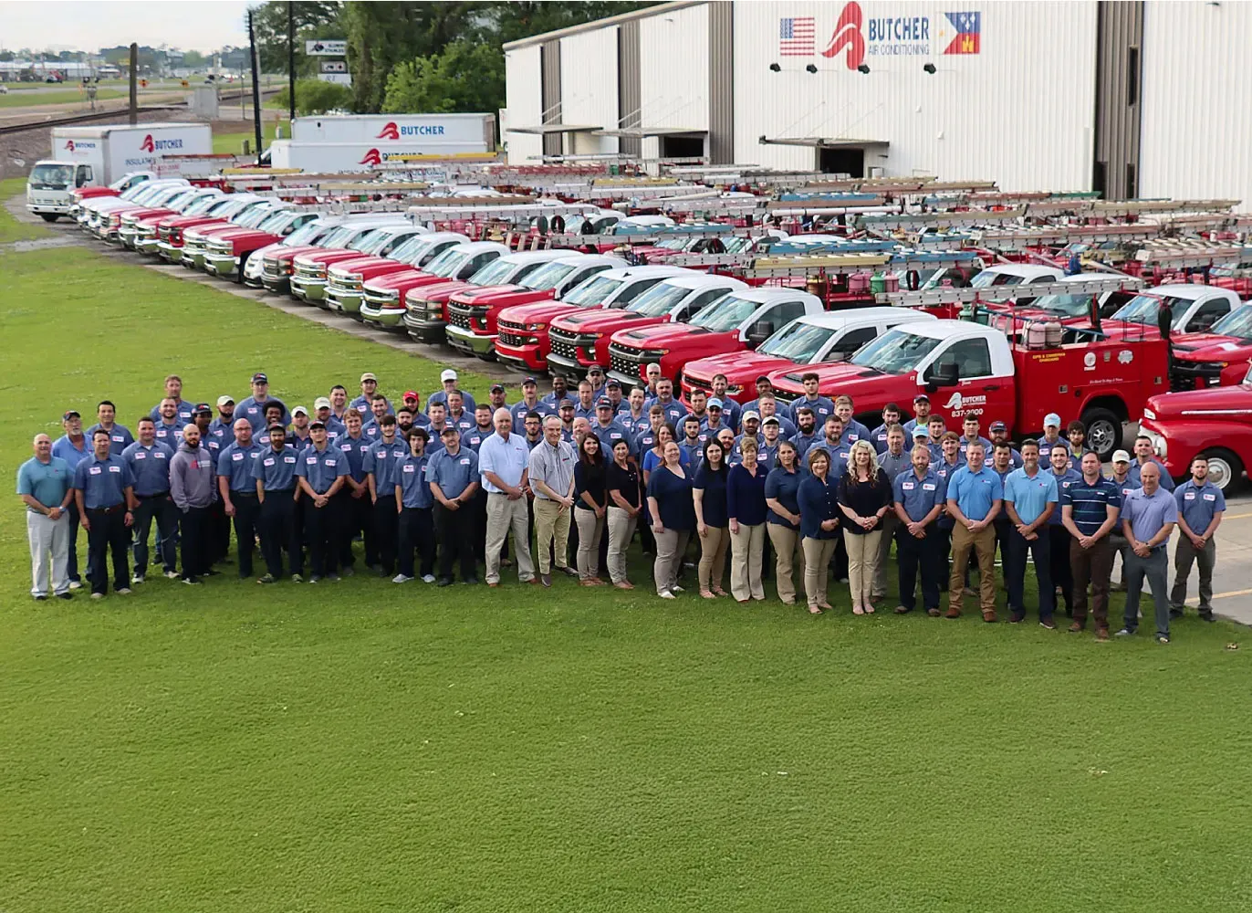 Butcher Air Conditioning HVAC team and staff posed in front of rows of red service trucks and company fleet