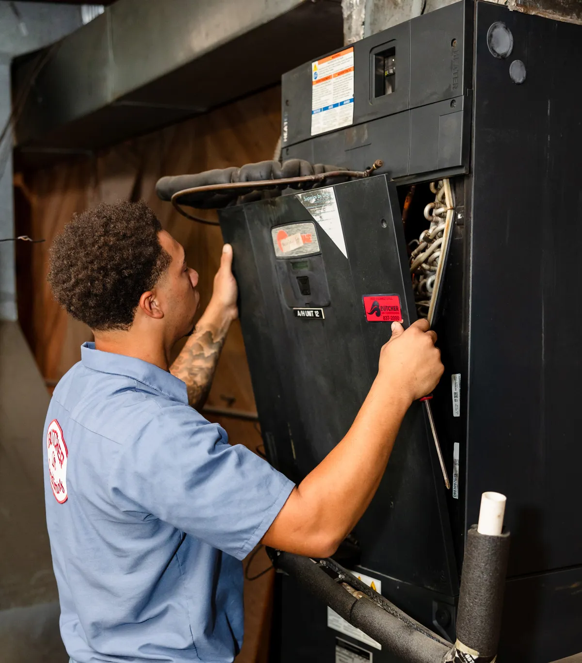 HVAC technician inspecting and repairing a commercial air handler unit with screwdriver
