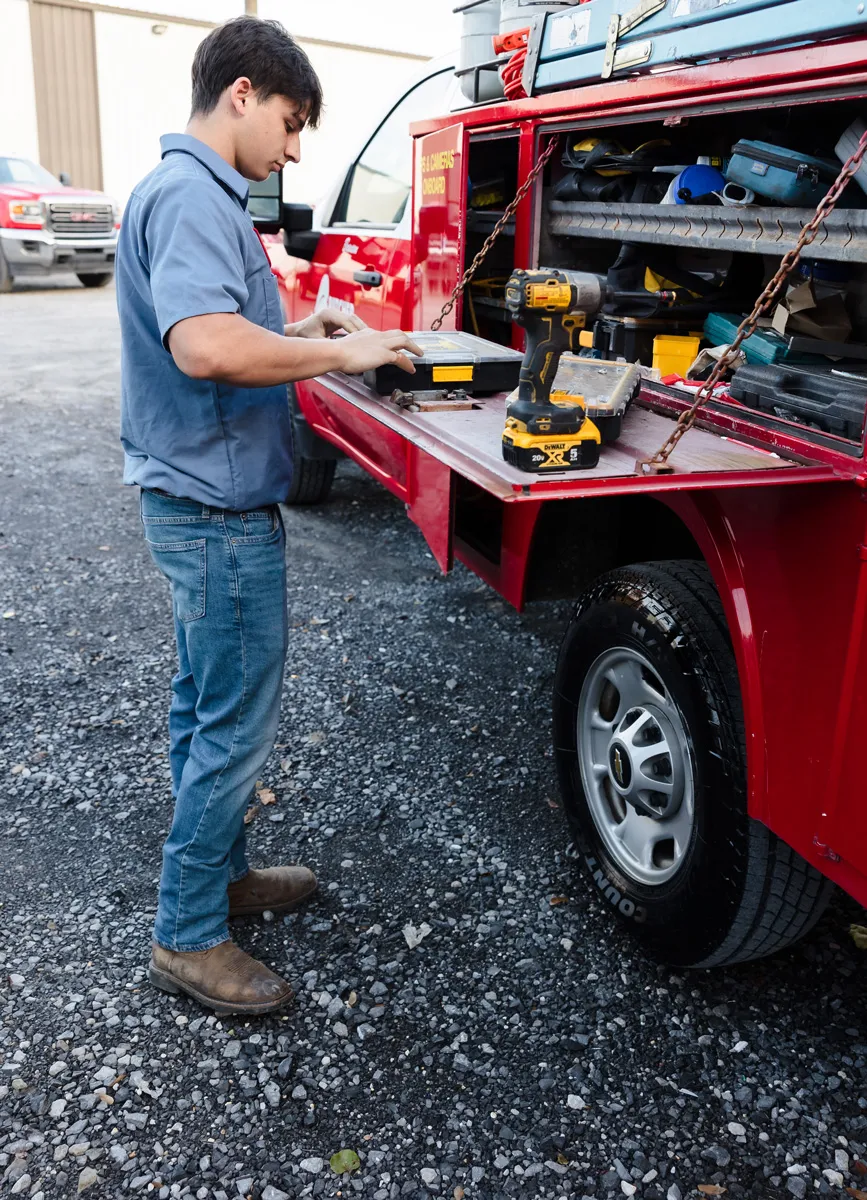 A man working at a red service truck’s side toolbench with cordless drill and toolbox, mobile mechanic preparing tools
