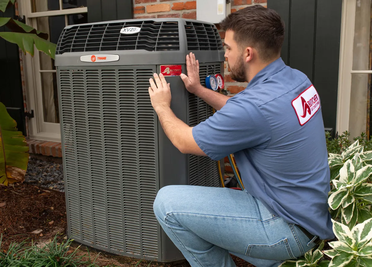 A technician inspecting a Trane outdoor air conditioning unit with gauges during residential HVAC maintenance