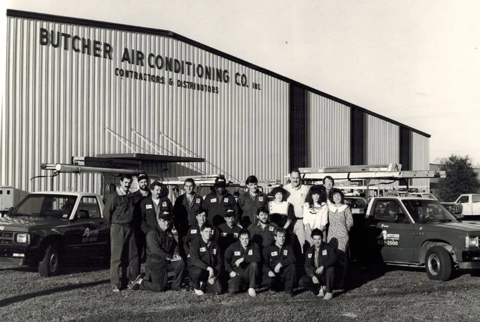 Butcher Air Conditioning team of technicians posed with service trucks and ladders outside company warehouse