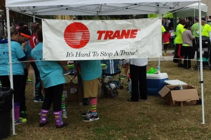 Trane banner on canopy at outdoor community event with people in bright shirts and colorful knee-high socks