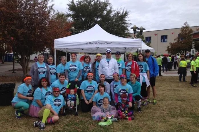 Team photo of people in matching blue shirts under white tent at community charity run
