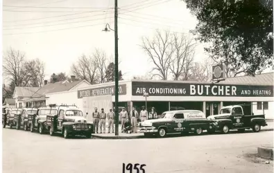 1955 vintage butcher and heating storefront with Air Conditioning sign, classic cars and people on sidewalk