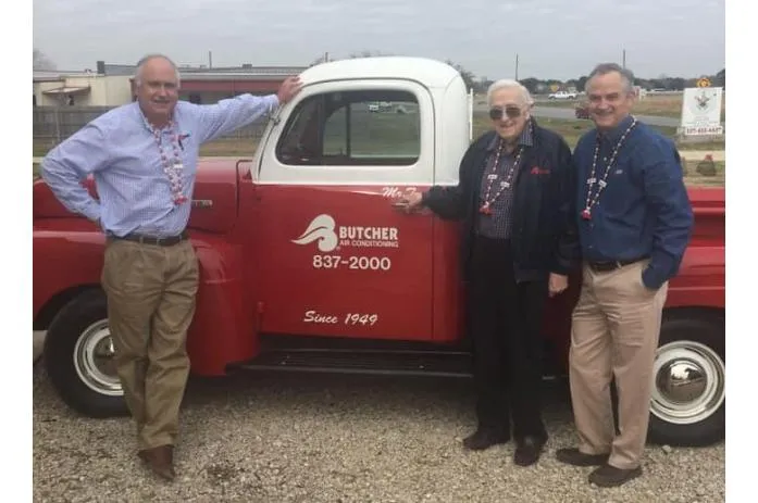 Three men posing beside vintage red Butcher Air Conditioning pickup truck with company logo and phone number