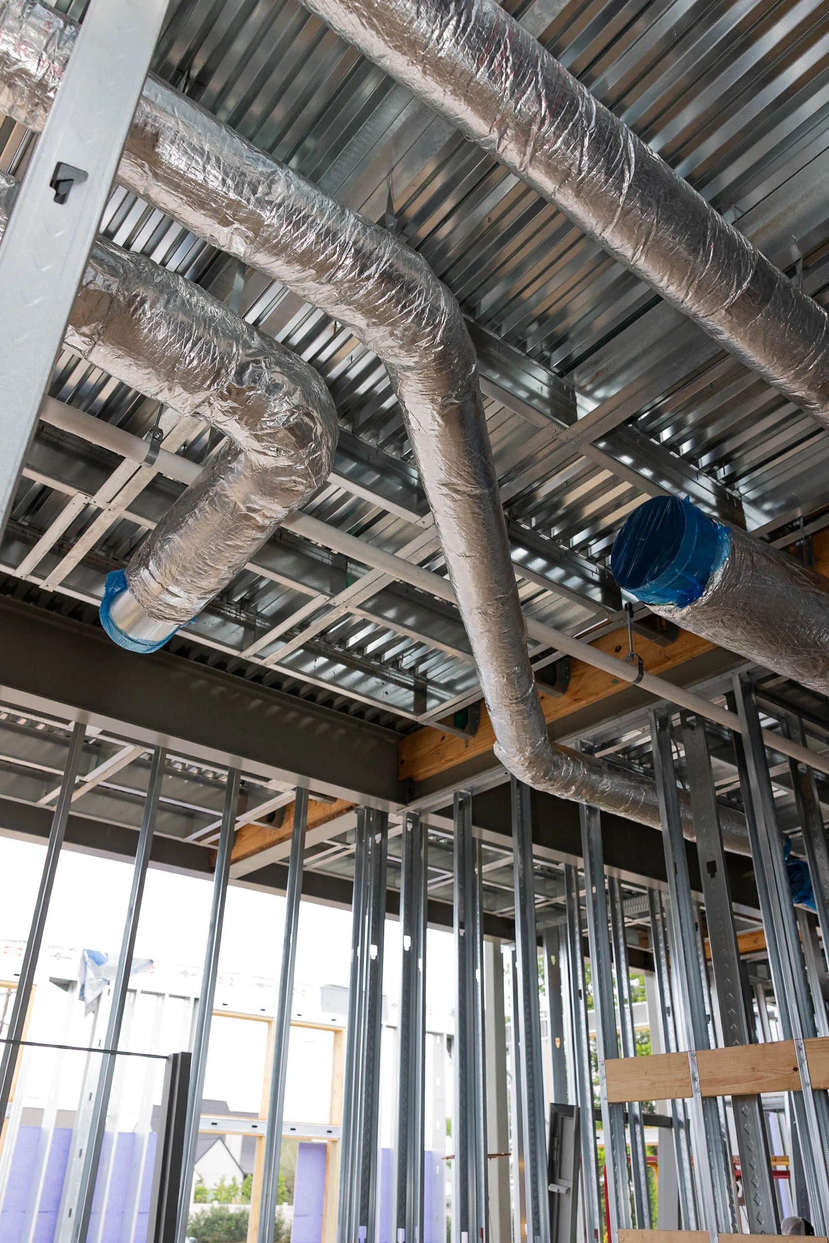 Interior construction with insulated foil-wrapped HVAC ducts and metal stud framing beneath corrugated steel deck