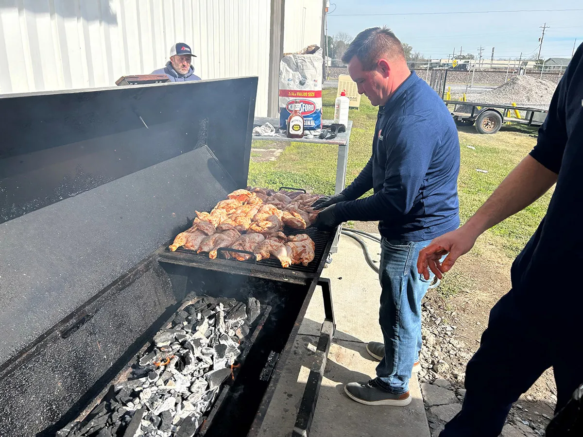 Man grilling seasoned chicken thighs on large charcoal smoker outdoors over hot coals for a backyard barbecue