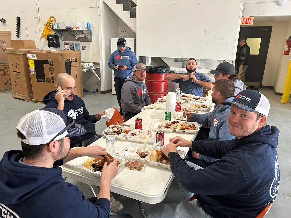 Warehouse workers eating barbecue lunch at folding table during break in industrial storage area