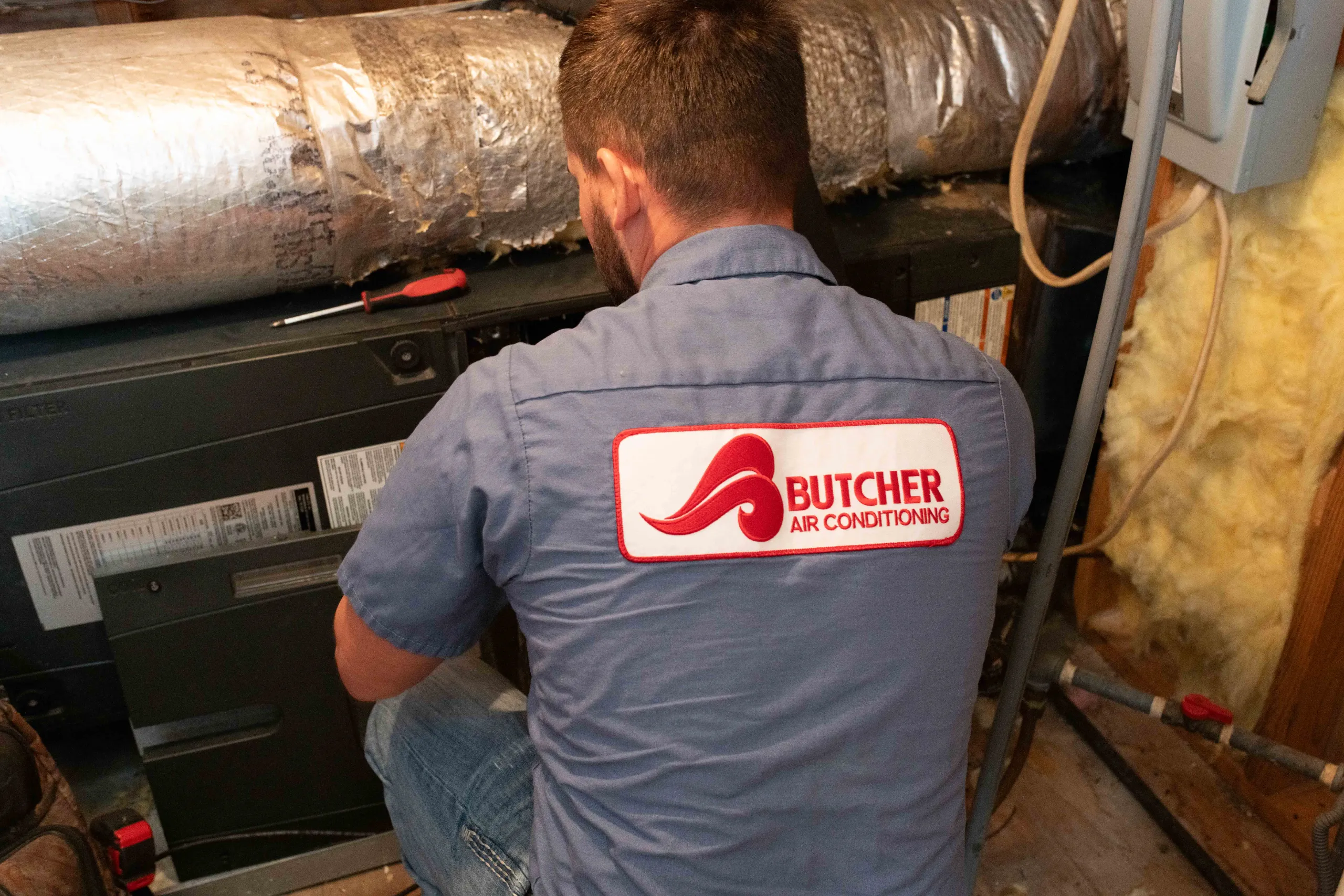 HVAC technician from Butcher Air Conditioning servicing furnace in attic with insulated ductwork