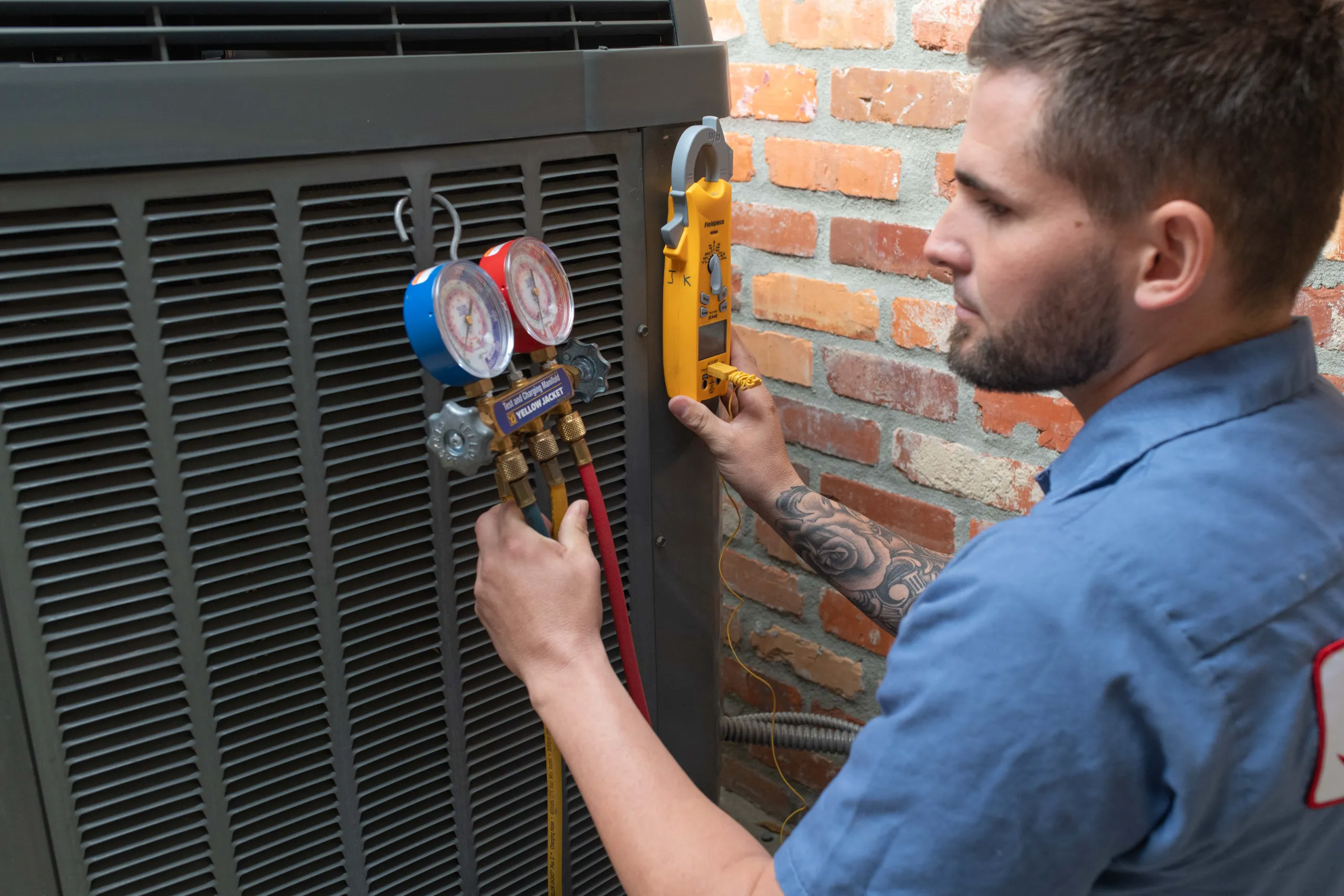 A man HVAC technician using manifold gauges and clamp meter to service an outdoor air conditioning unit