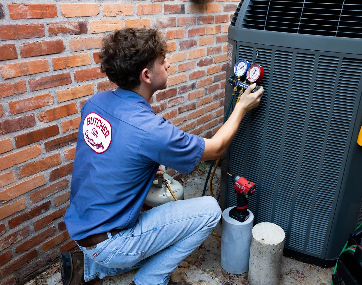 A man HVAC tech checking pressure gauges on outdoor air conditioning unit beside brick wall