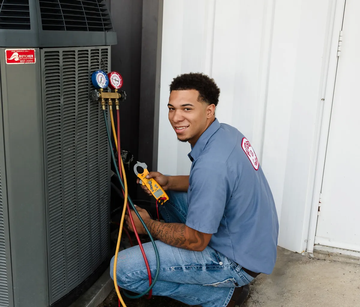 A man HVAC technician kneeling by outdoor air conditioner using manifold gauges and clamp meter to check refrigerant levels