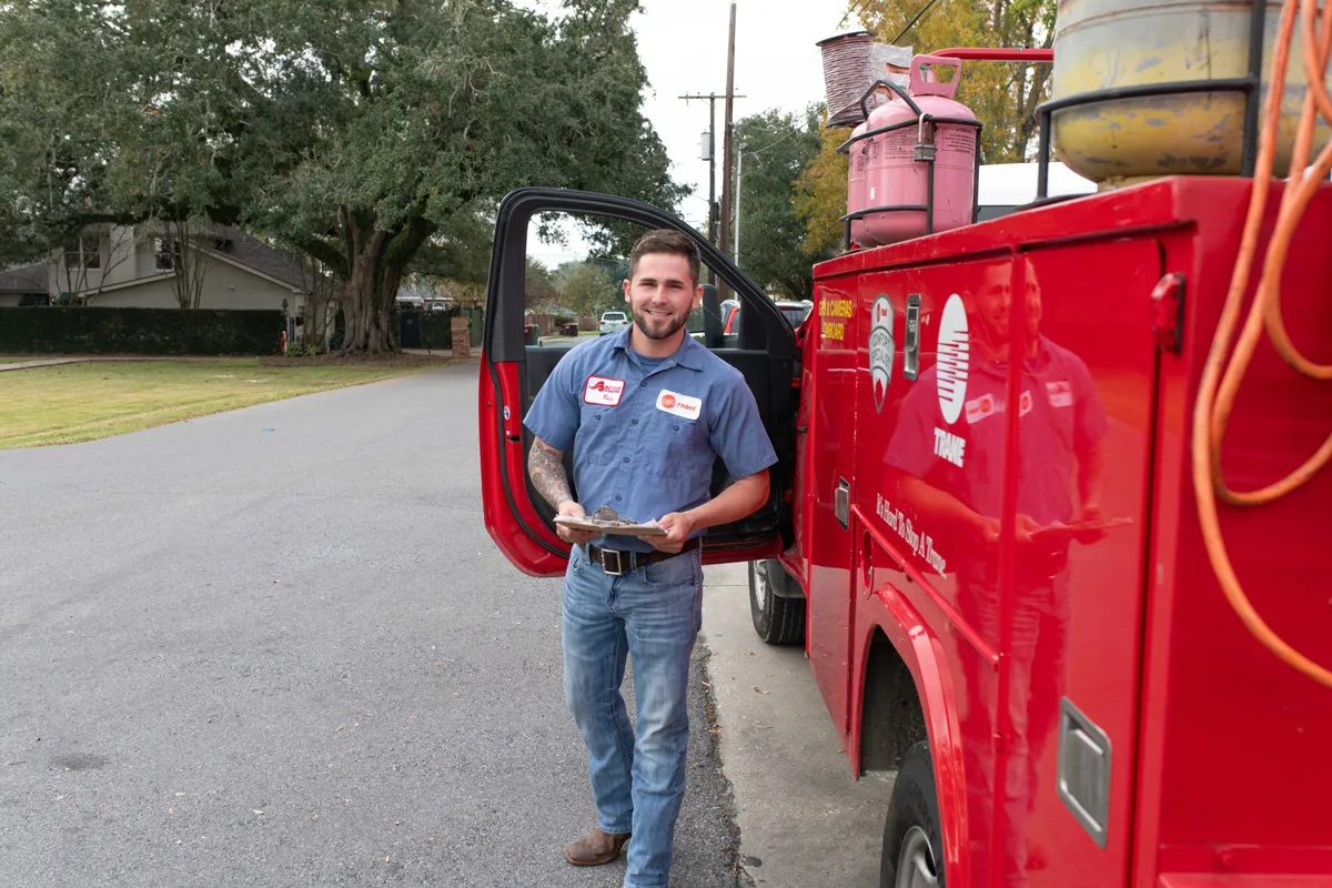 Smiling man in work uniform with clipboard standing by red service truck on suburban street