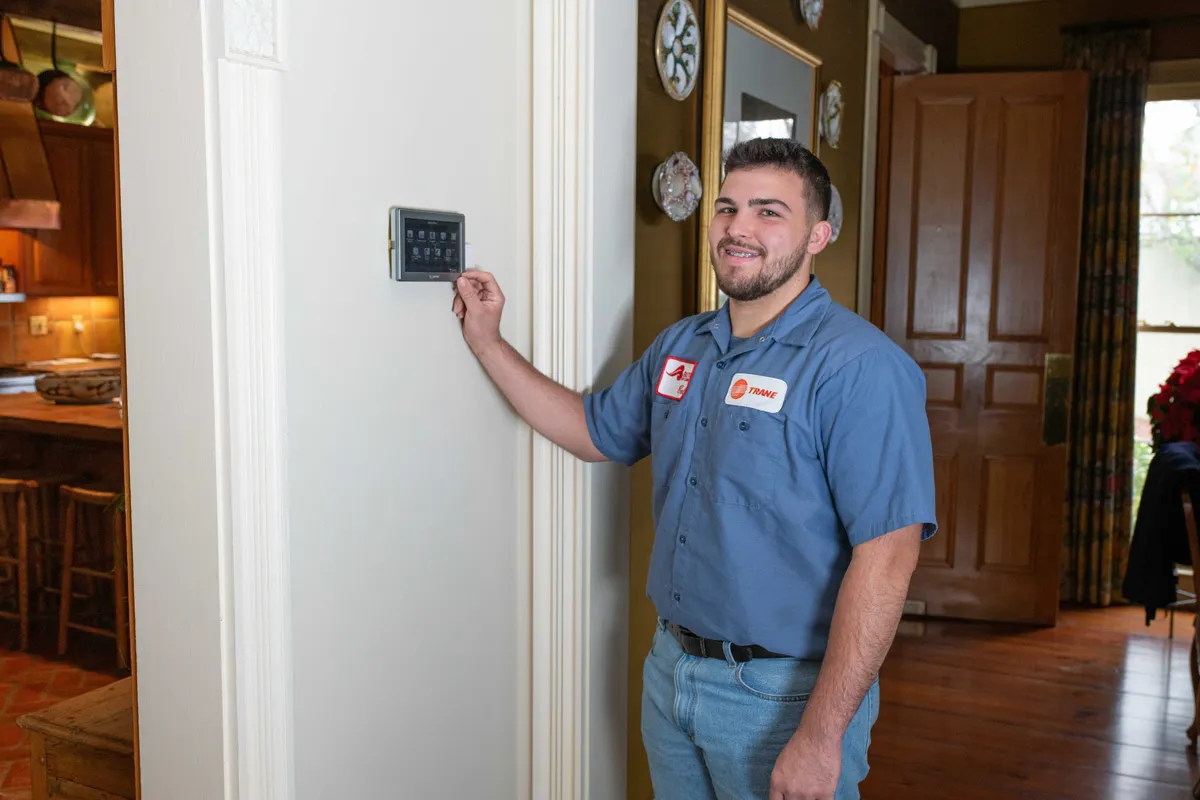 HVAC technician installing a wall-mounted smart thermostat in a home's entryway