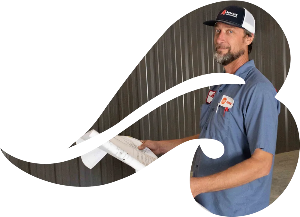 A man in a blue work shirt and cap holding paperwork inside a metal-sided warehouse, looking at camera