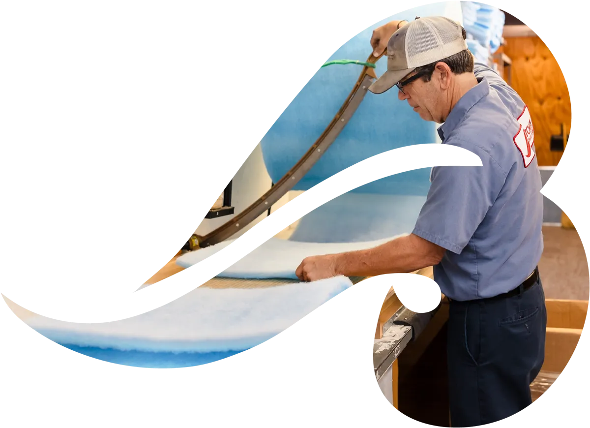 A man trimming blue foam batting with a curved industrial cutter for upholstery or mattress production.