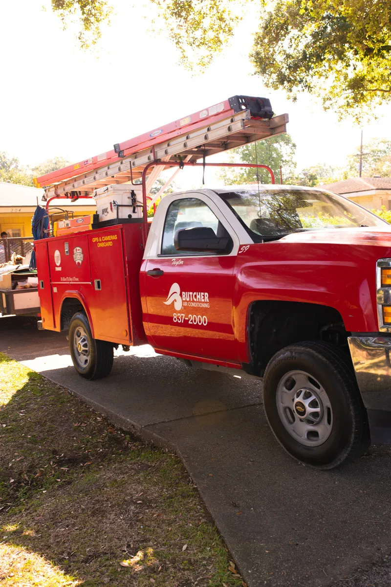 Red Butcher Air Conditioning service truck with ladder and equipment parked in a residential driveway