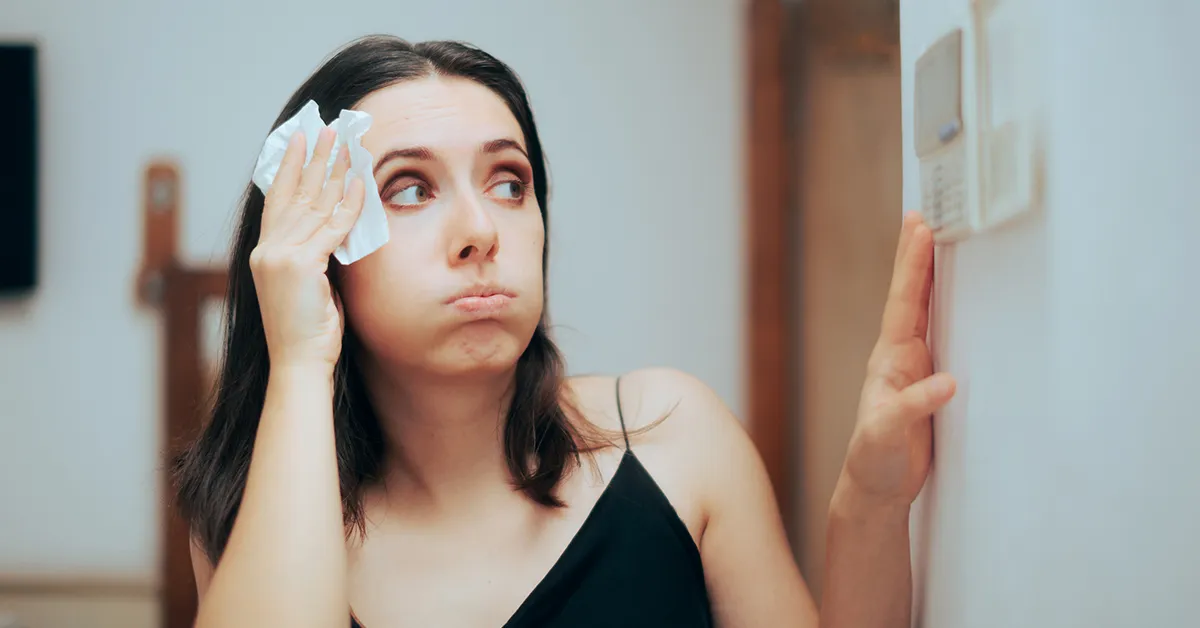 A woman checking her thermostat and dabbing her forehead during a Louisiana heatwave.