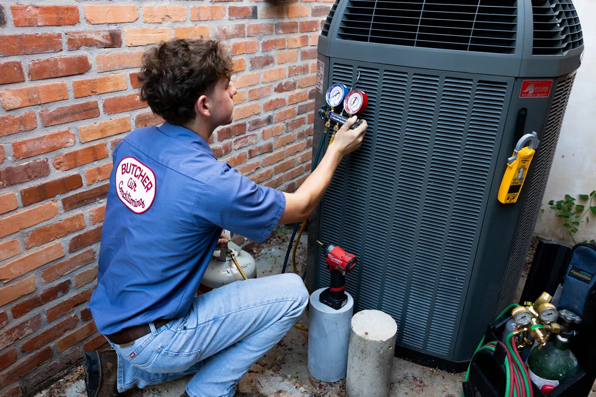 HVAC technician kneeling at outdoor air conditioner using manifold gauges for diagnostics