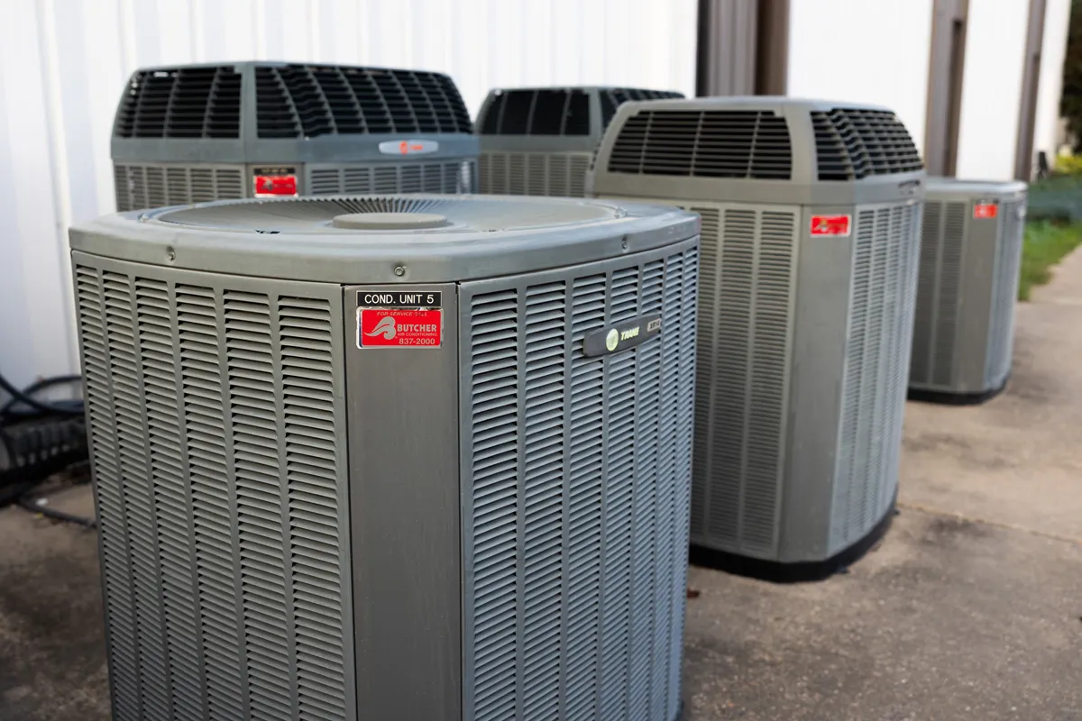 Multiple outdoor commercial HVAC air conditioning condenser units lined up beside a building