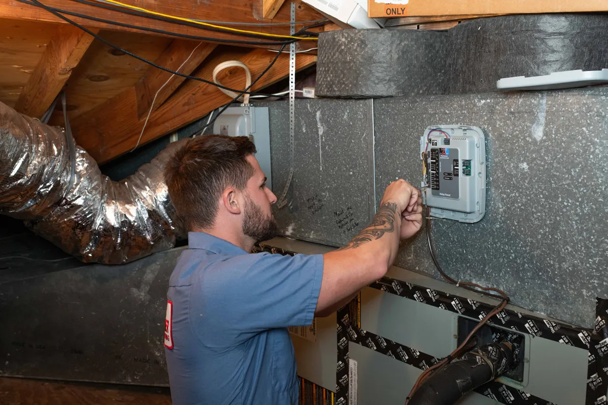 A man installing HVAC control module on metal ductwork in attic, HVAC technician at work
