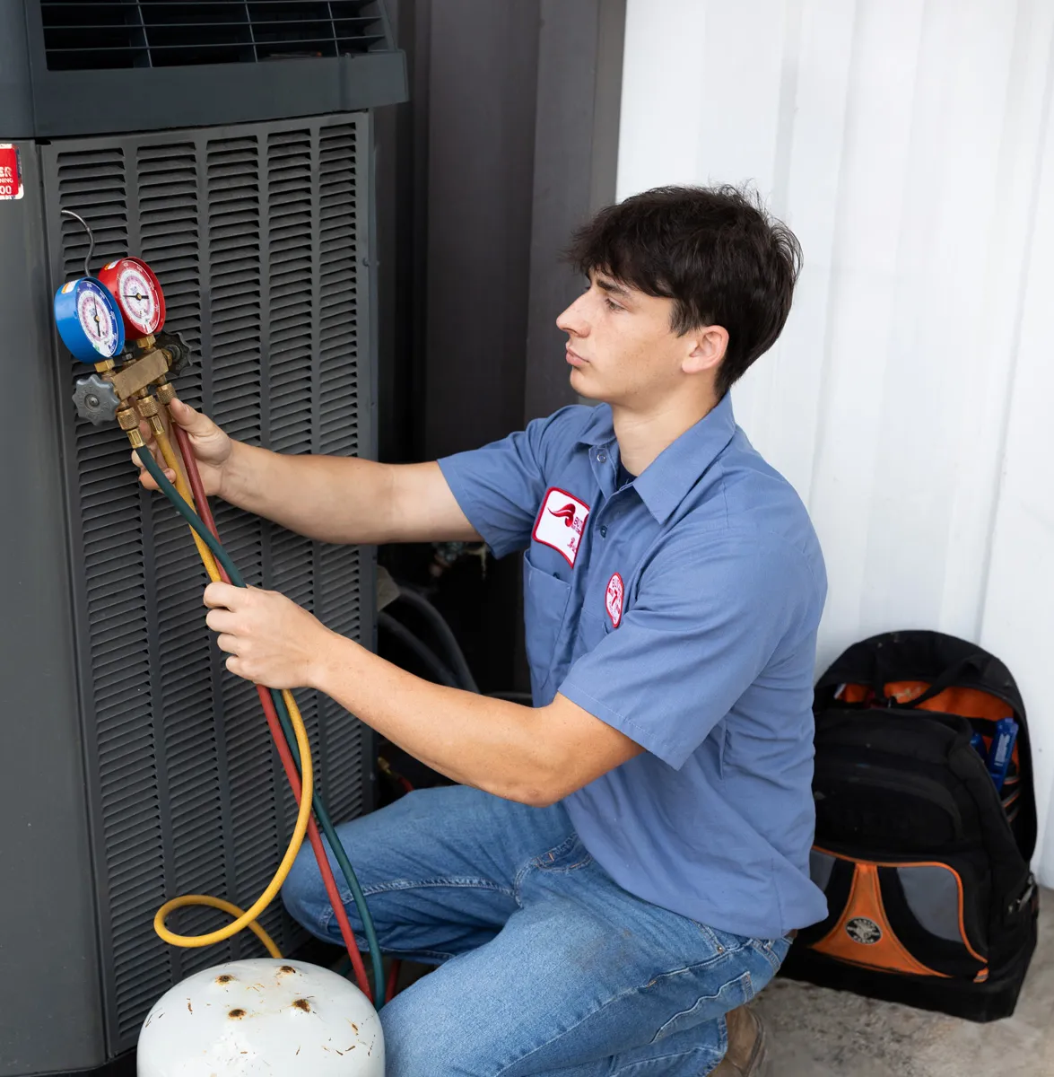 A man checking HVAC refrigerant pressure with manifold gauges on an outdoor air conditioner