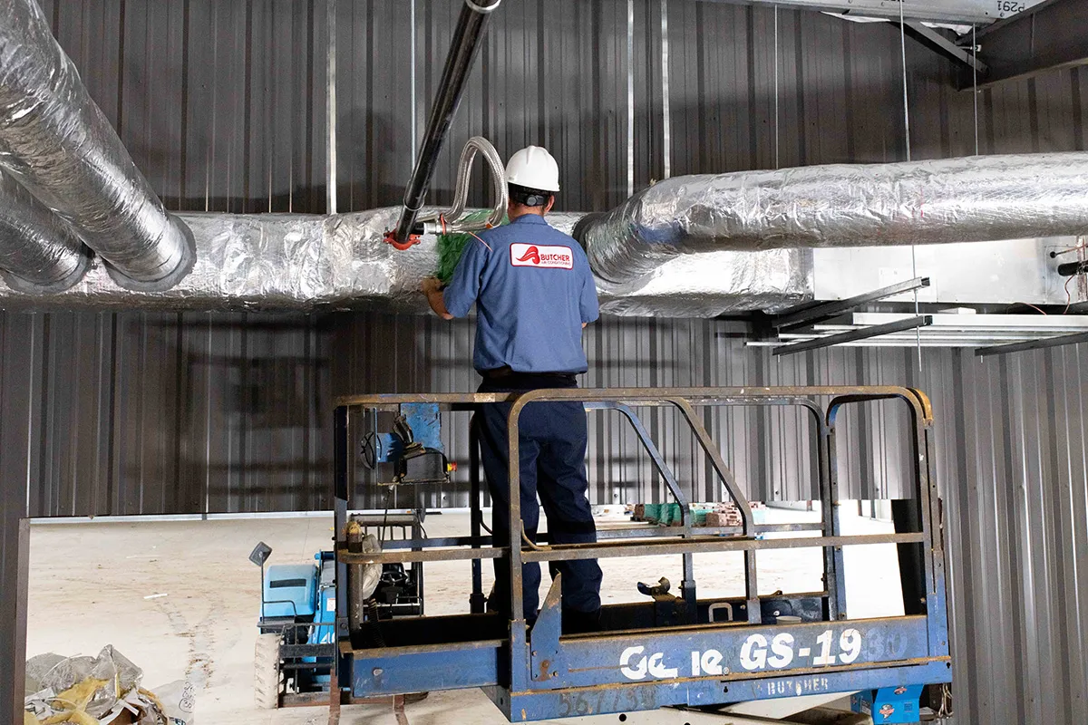 Worker on scissor lift installs insulated HVAC ductwork in industrial warehouse interior