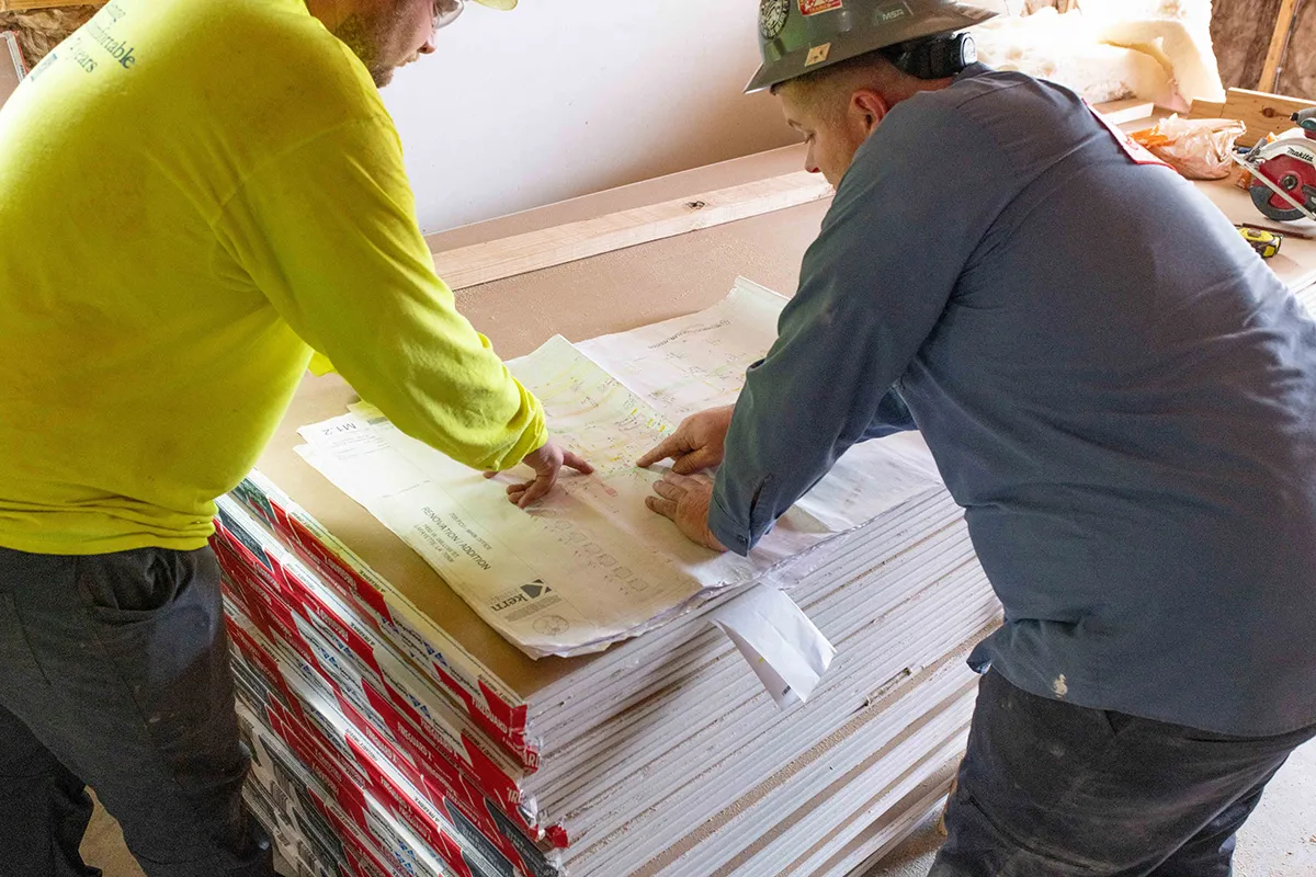 Construction workers examining blueprints on a stack of drywall at a renovation job site