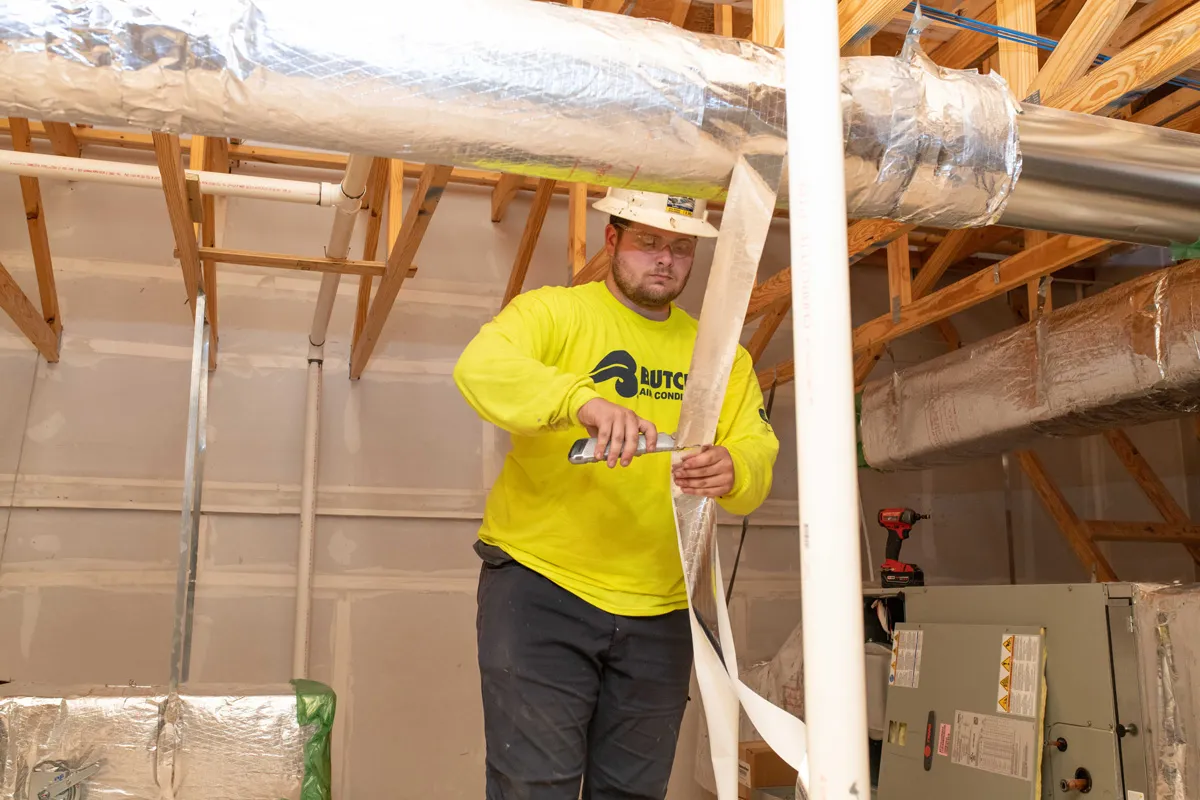 HVAC technician installing reflective duct insulation in attic during residential ductwork installation