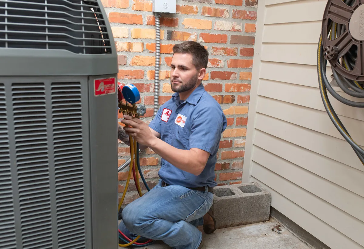HVAC technician kneeling by an outdoor air conditioner, checking manifold gauges during residential AC service