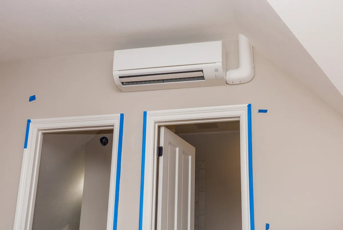 Wall-mounted ductless mini-split air conditioner above two doorways with blue painter's tape on beige interior wall