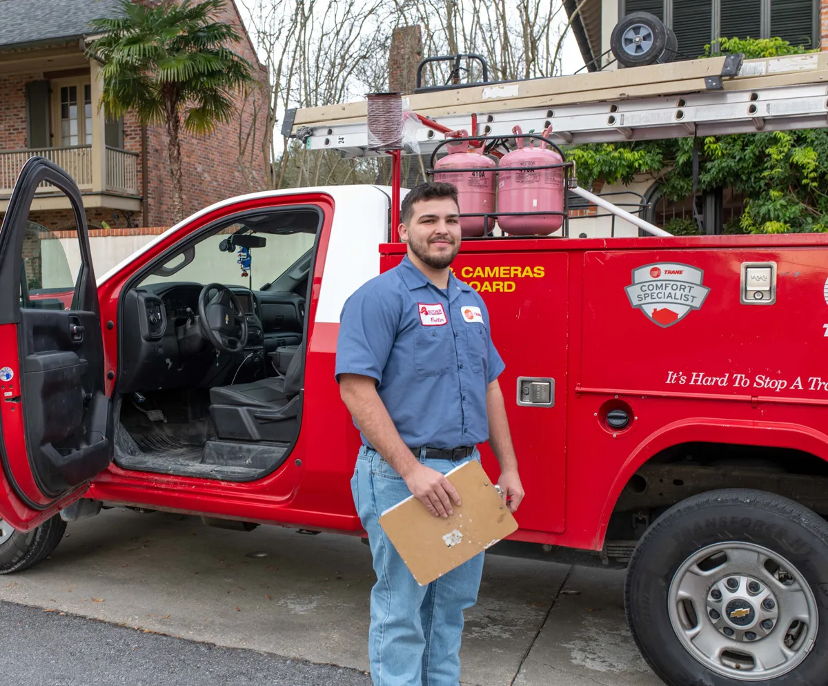 HVAC technician standing by red service truck holding clipboard in residential driveway
