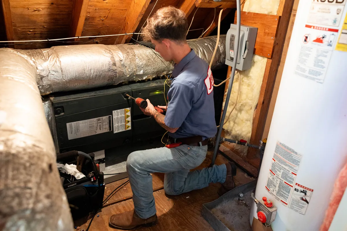 Man repairing HVAC unit in attic with power drill beside water heater