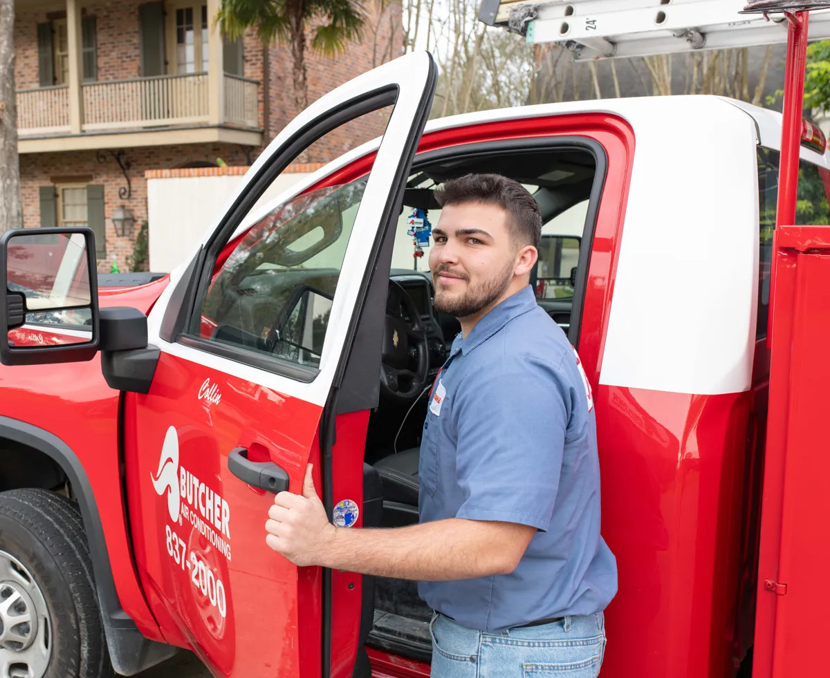 Man in blue work shirt opening door of red Butcher Air Conditioning service truck with ladder on top