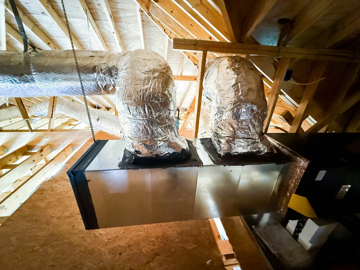 Foil-insulated HVAC ductwork and metal plenum in unfinished attic with exposed wooden rafters
