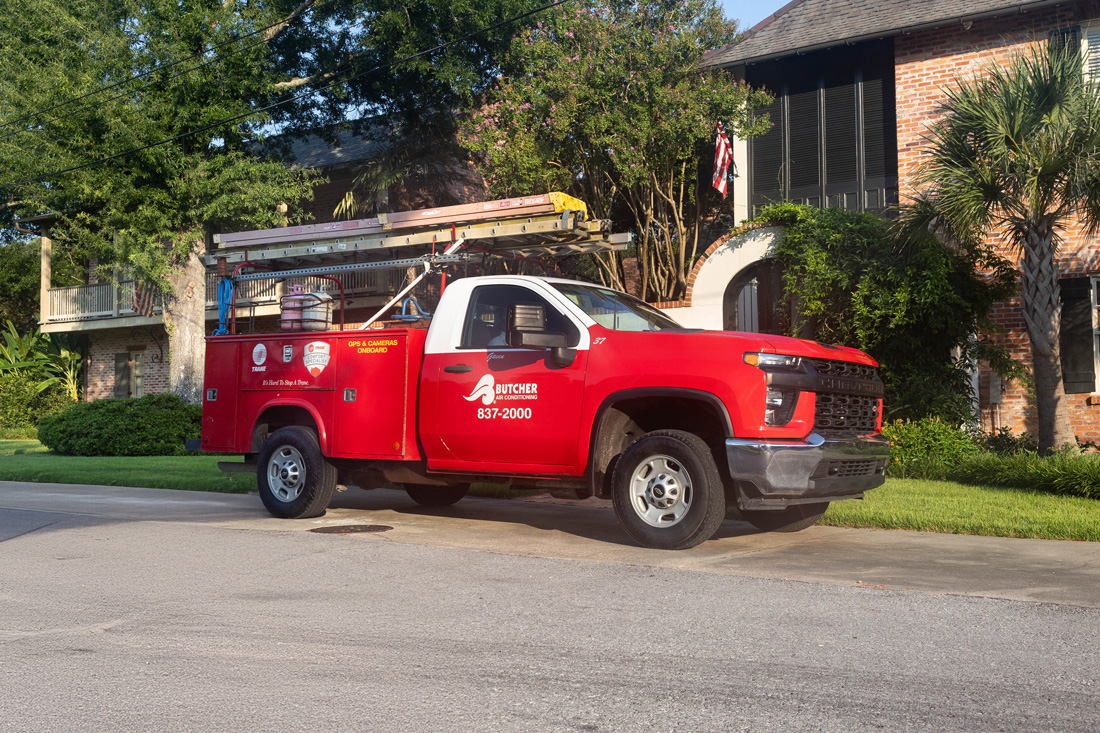 Two HVAC technicians standing beside a red Butcher Air Conditioning service truck with ladders