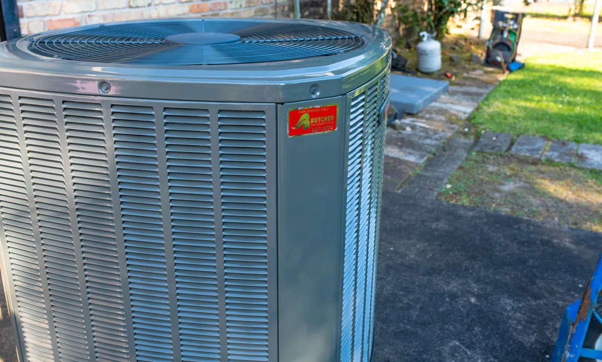 Outdoor residential central air conditioner condenser unit HVAC with top fan on driveway beside lawn