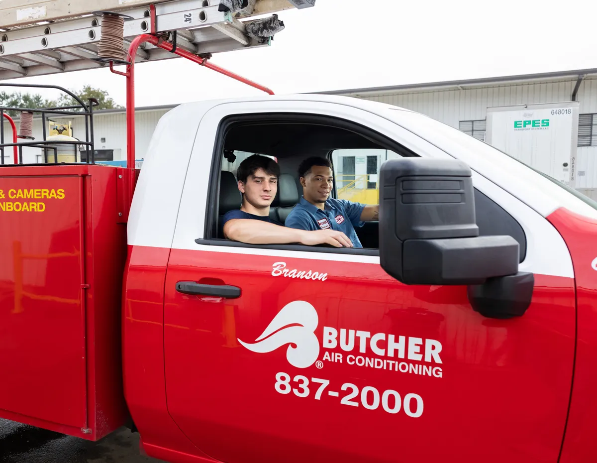 Two HVAC technicians in red Butcher Air Conditioning service truck with ladder, ready for repair