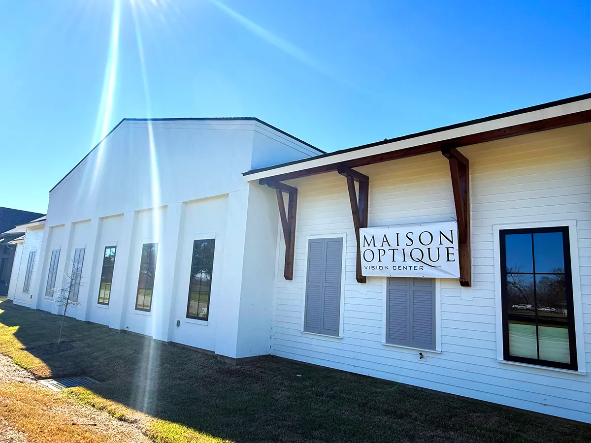 Exterior of Maison Optique Vision Center: modern white building with wooden awnings, windows, sunny blue sky.