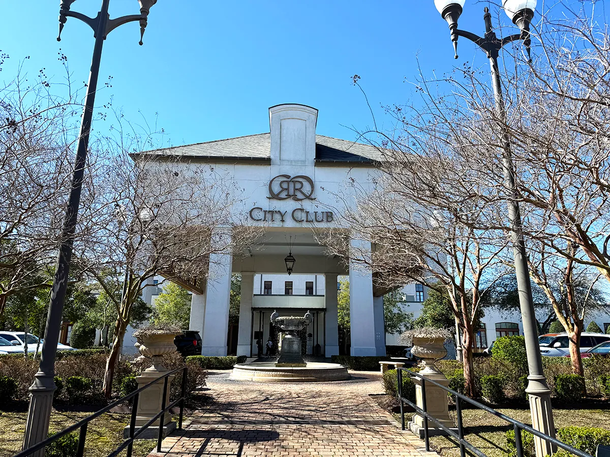 City Club building entrance with central fountain, brick walkway, lamp posts and leafless trees under clear blue sky