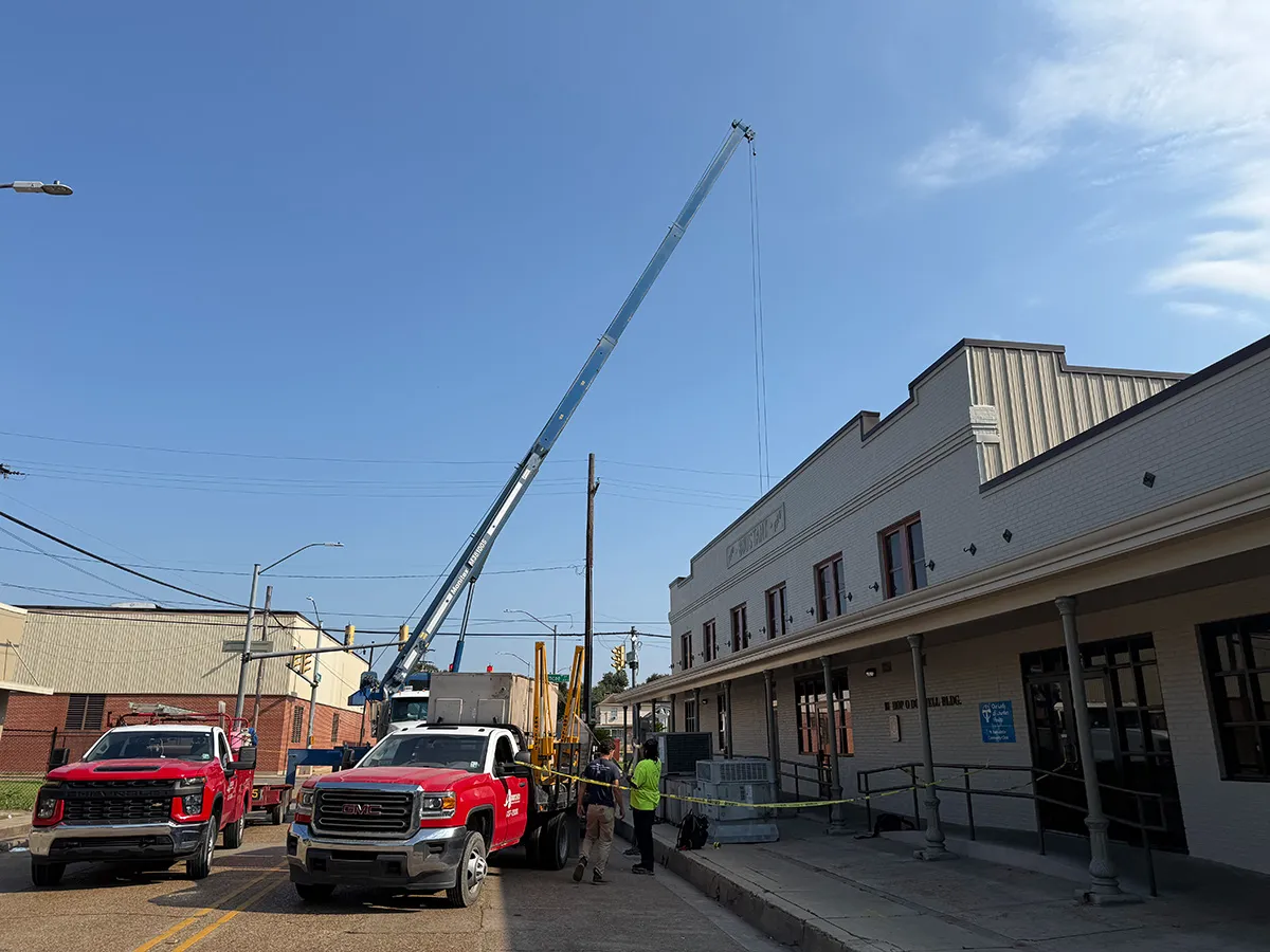 Utility crane and red service trucks with workers beside a historic brick building under clear blue sky