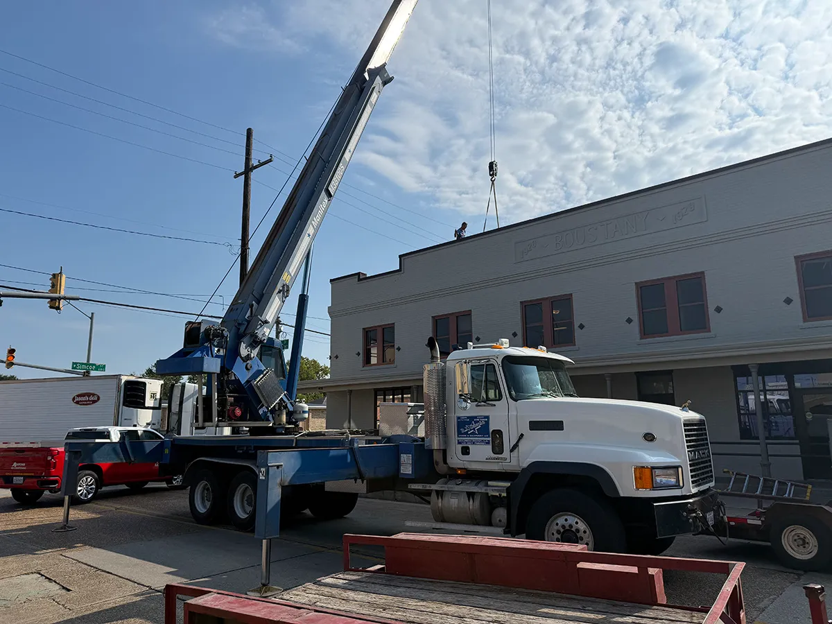 Mobile crane truck lifting equipment to a downtown building rooftop with a worker on the roof