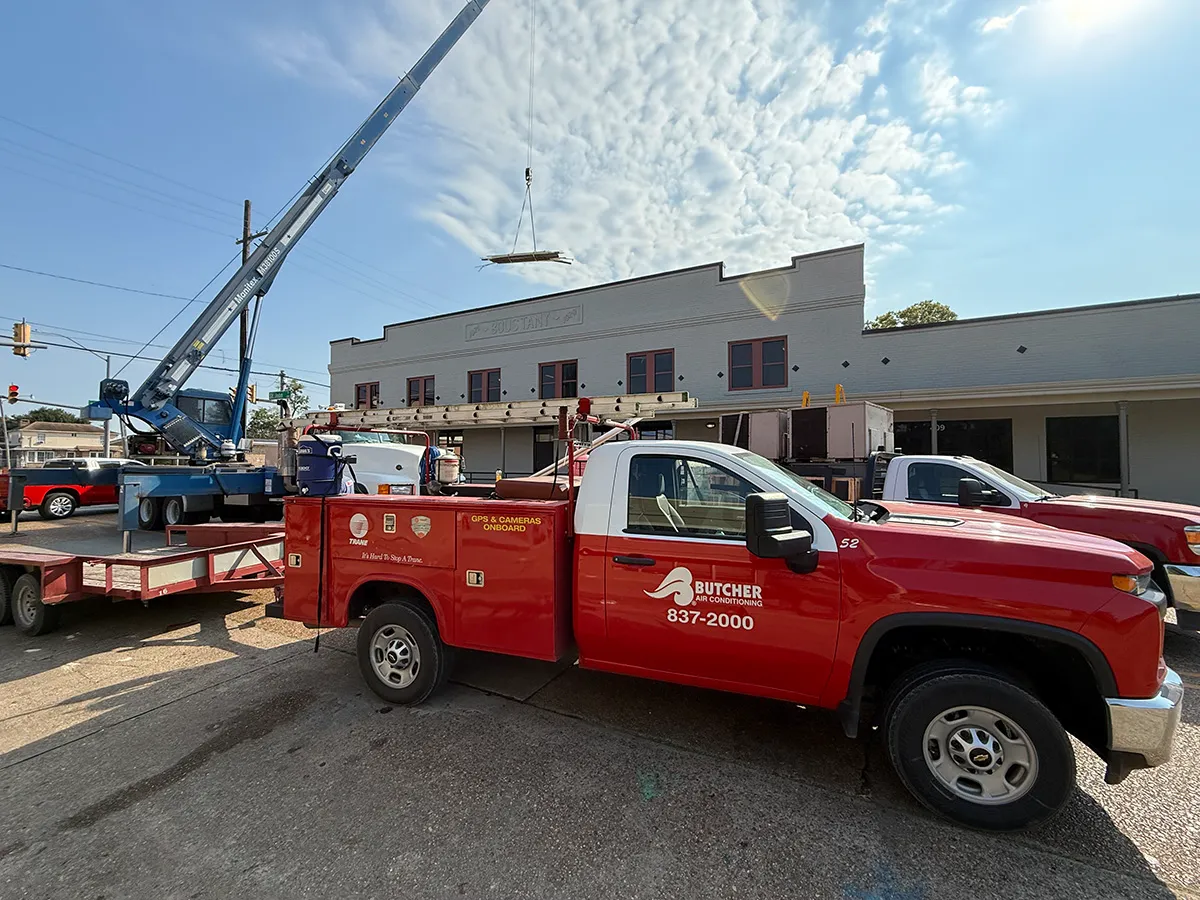 Red Butcher Air Conditioning HVAC service truck beside crane lifting rooftop materials at storefront renovation site