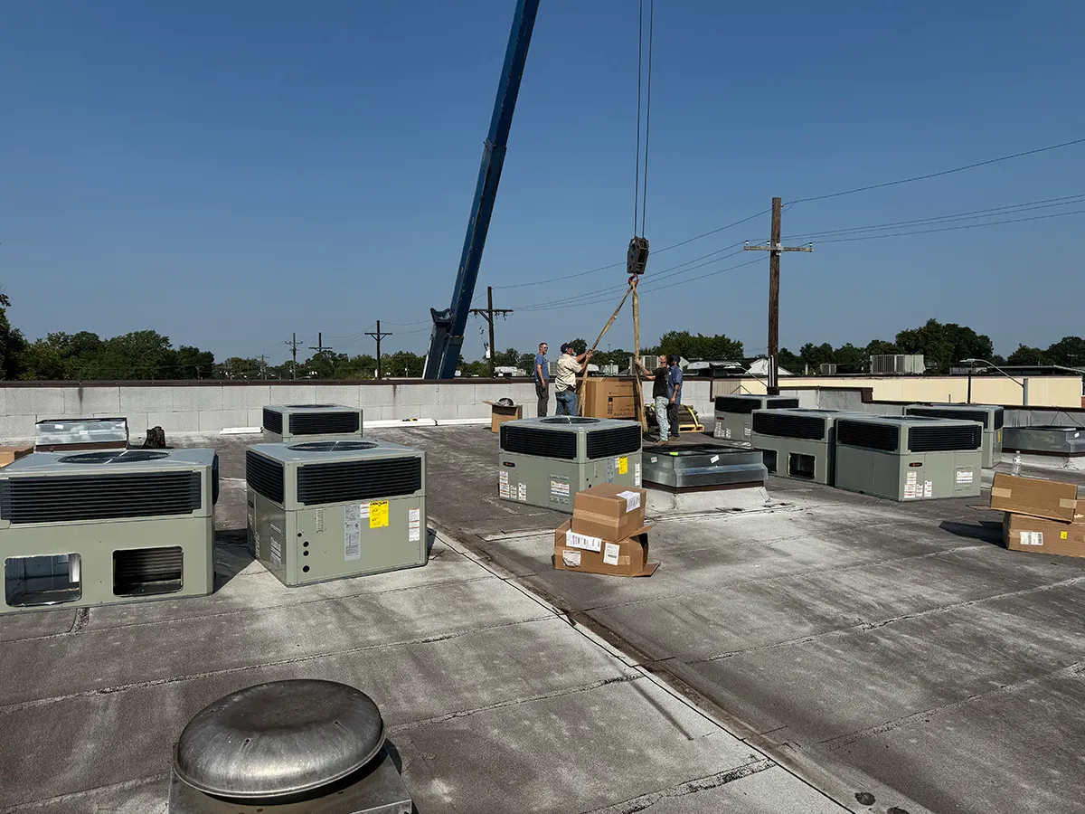 Technicians using crane to lift HVAC unit onto commercial rooftop during HVAC installation with multiple units