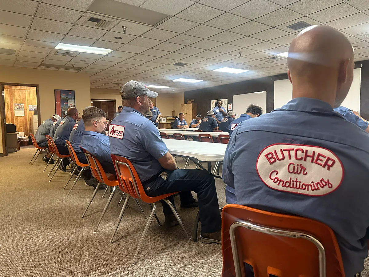 Group of technicians in Butcher Air Conditioning uniforms at an HVAC team meeting in a break room