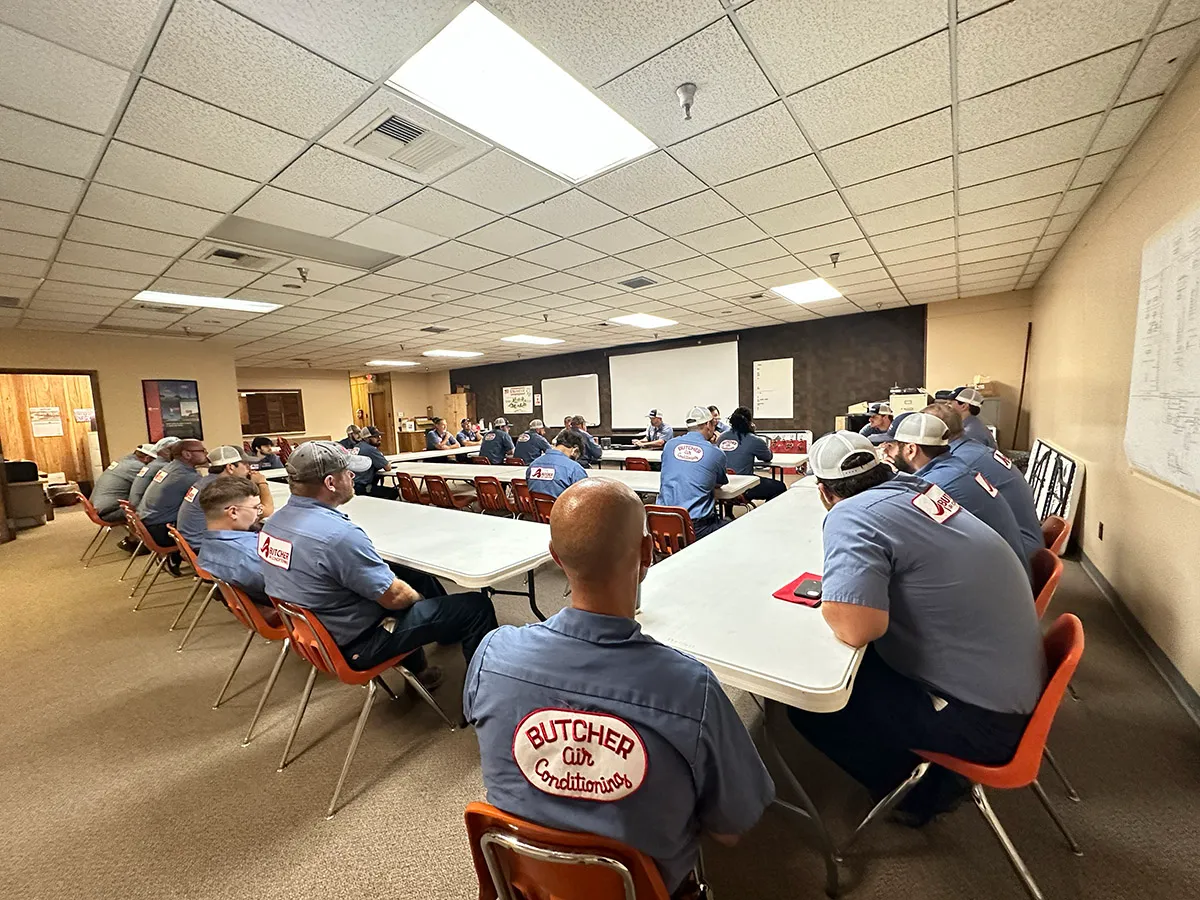 HVAC technicians in blue Butcher Air Conditioning shirts attending a training meeting in a conference room