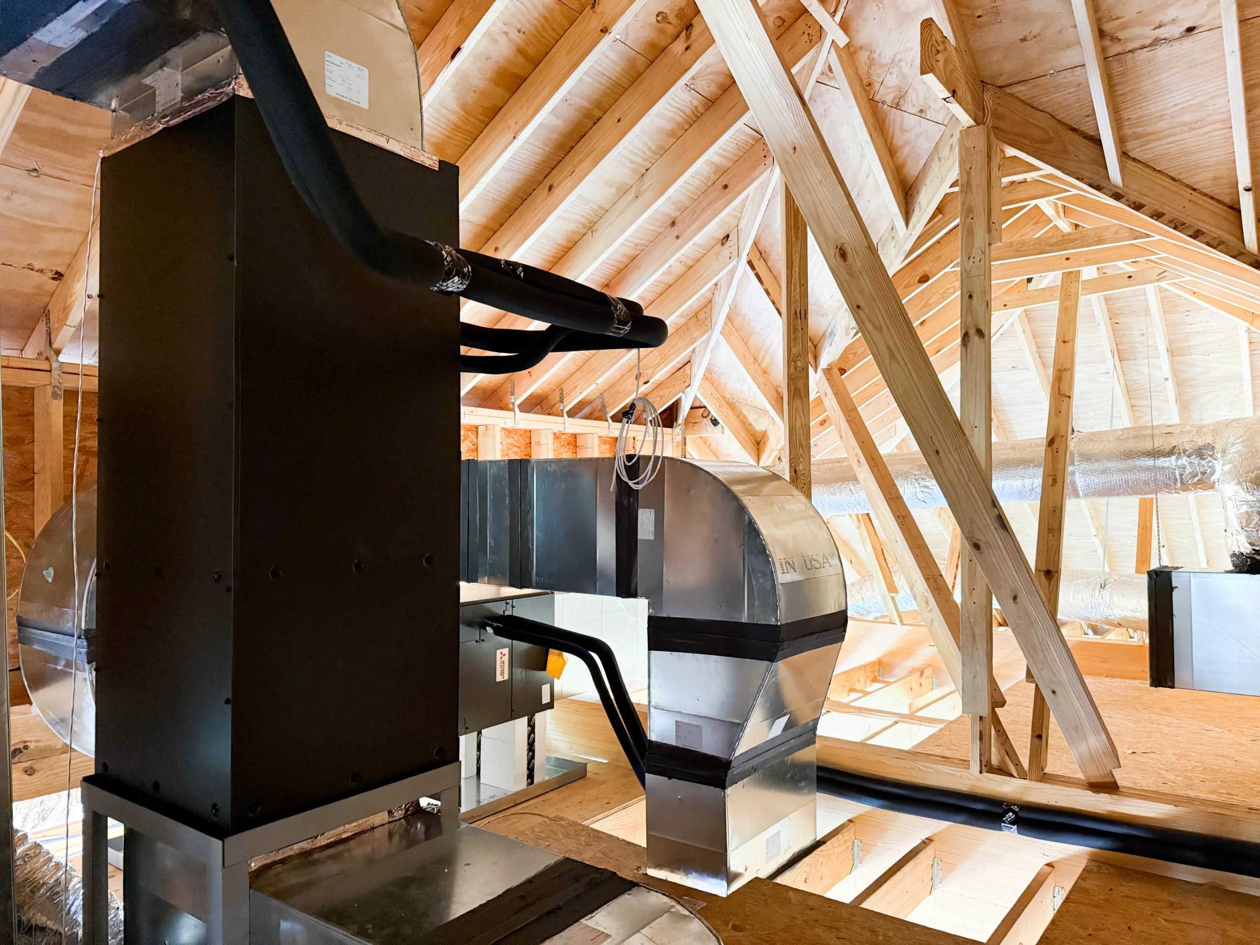 Attic HVAC installation with metal ductwork, insulated black refrigerant lines and exposed wooden rafters