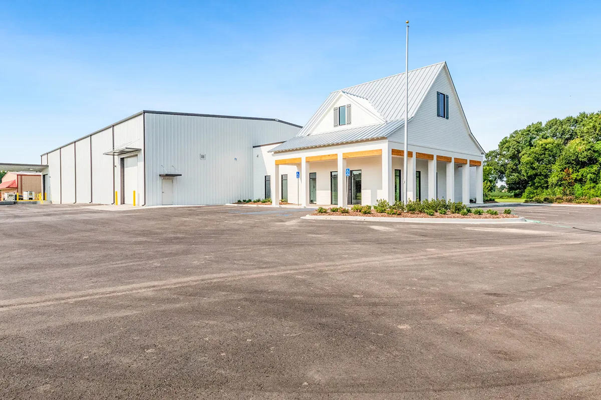New white commercial office with adjacent metal warehouse, large paved parking lot and landscaping under clear blue sky