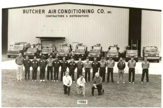 Butcher Air Conditioning Co. team (1990) standing in front of company building with service trucks lined up.